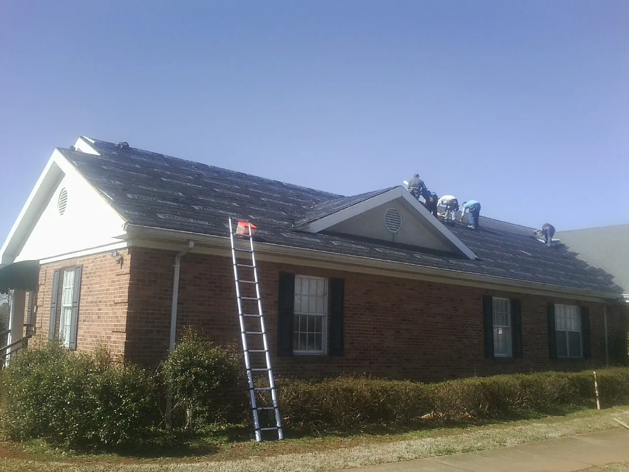 Crew tearing shingles off a brick ranch roof with a ladder set — Emergency Roof Repair work by our crew in Princess Anne