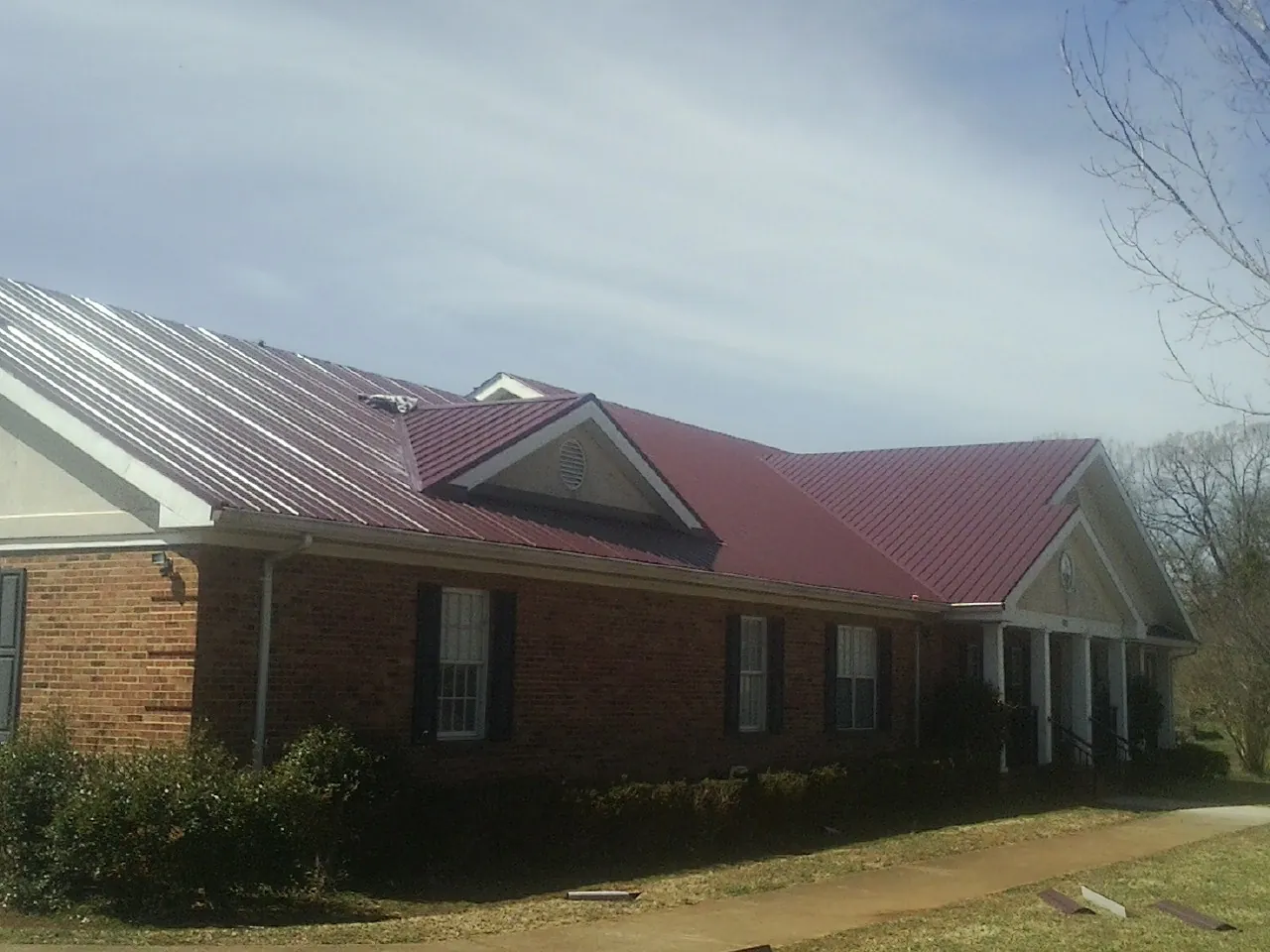 Red metal roof with gabled entries on a long brick building, from a Hail Damage Roof Repair job in Princess Anne