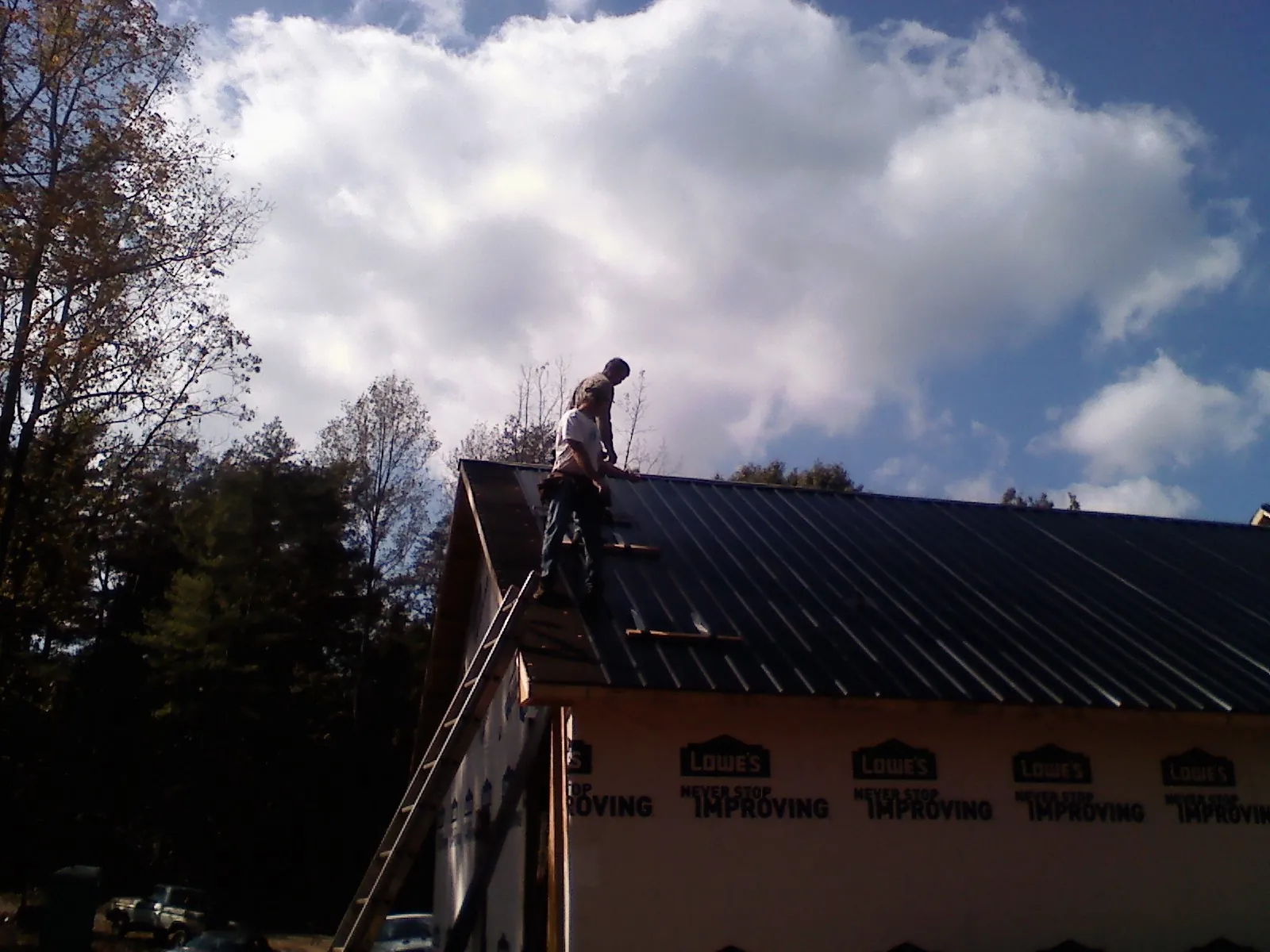 Roofer fastening dark metal panels high against a cloudy sky, from a Roof Inspection job in Princess Anne