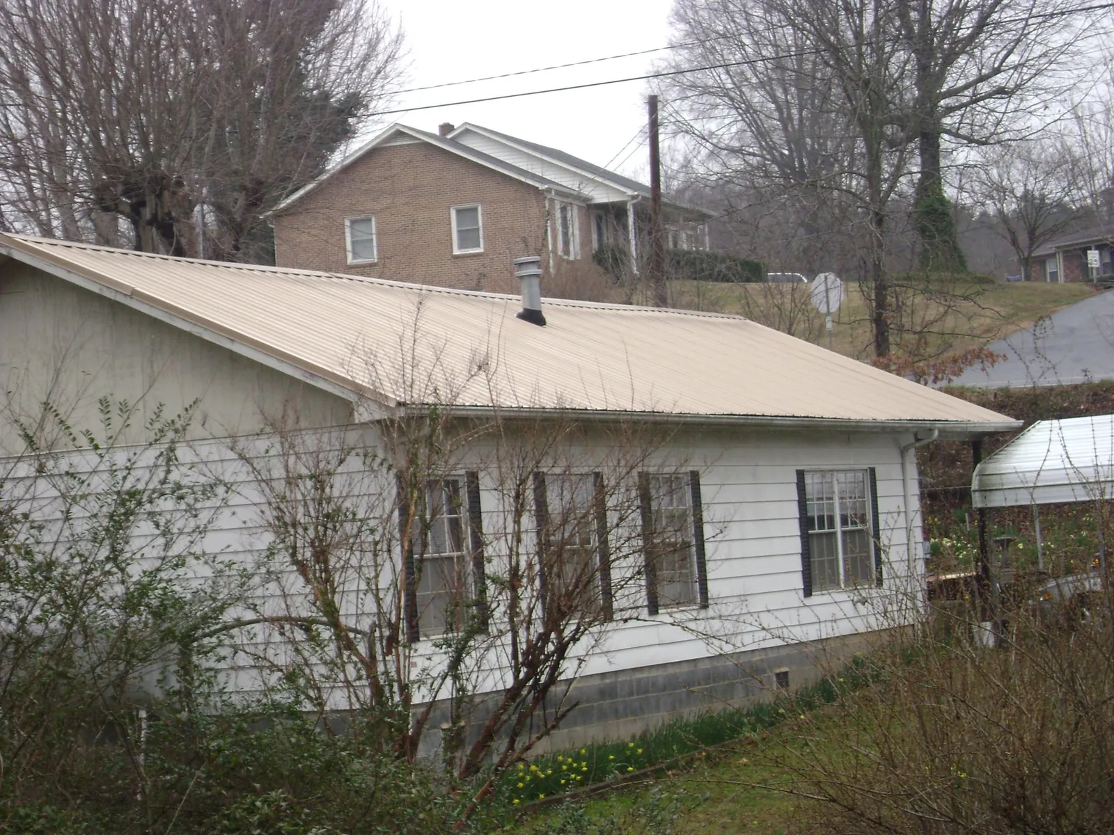 Tan metal roof on a white sided house set into a hillside — Commercial Roofing by Roofing Brothers in Princess Anne
